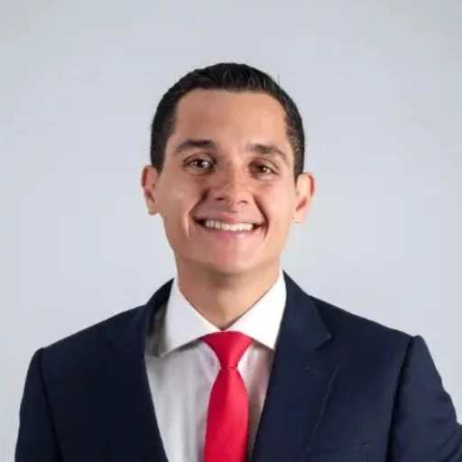 Portrait of Ivan Padron, Admissions Manager at Ascencia Malta, smiling in a navy suit, white shirt, and red tie